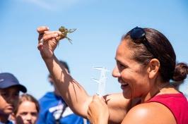 Woman in red shirt holds up a crab and smiles at it